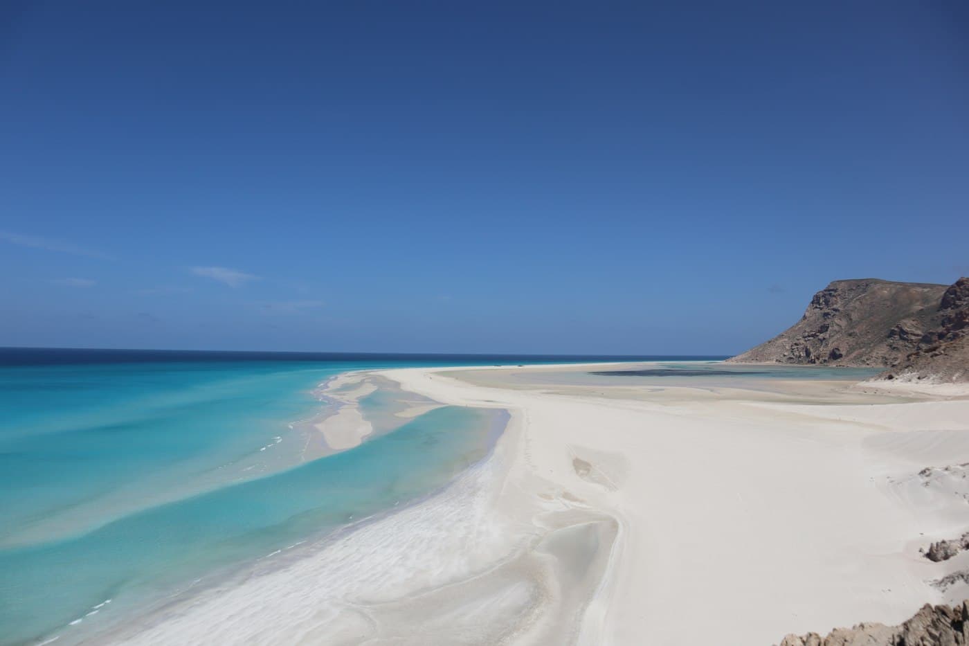 Turquoise ocean meets white sand beach with rocky hills